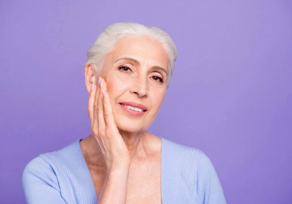 A woman with white hair is holding her face.